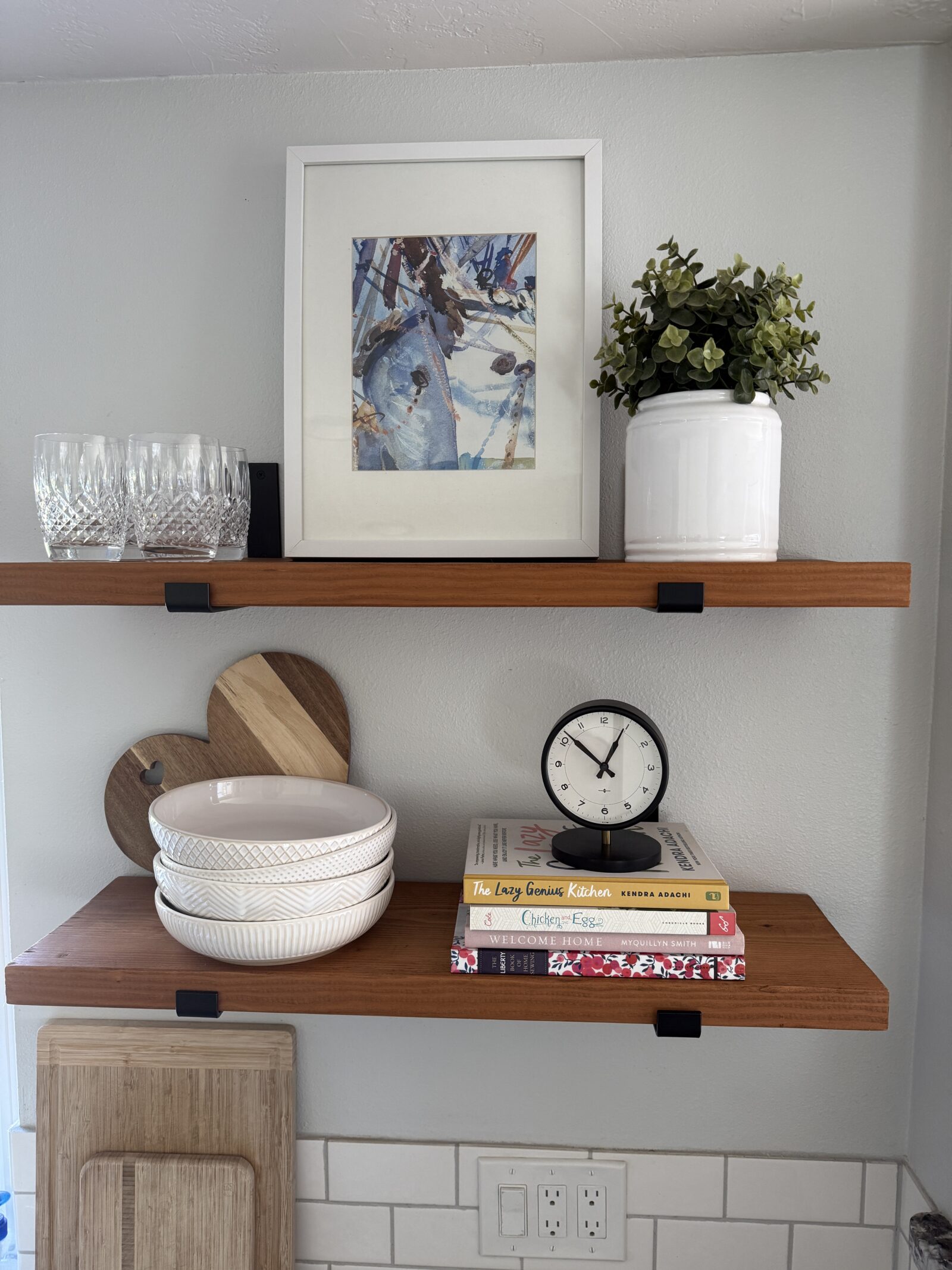 Wood shelves decorated for spring with artwork, bowls, a plant, and a stack of books.