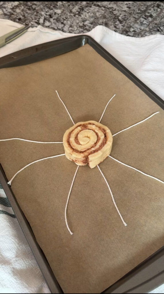 A raw cinnamon roll laid on top of 5 pieces of kitchen twine in a star shape