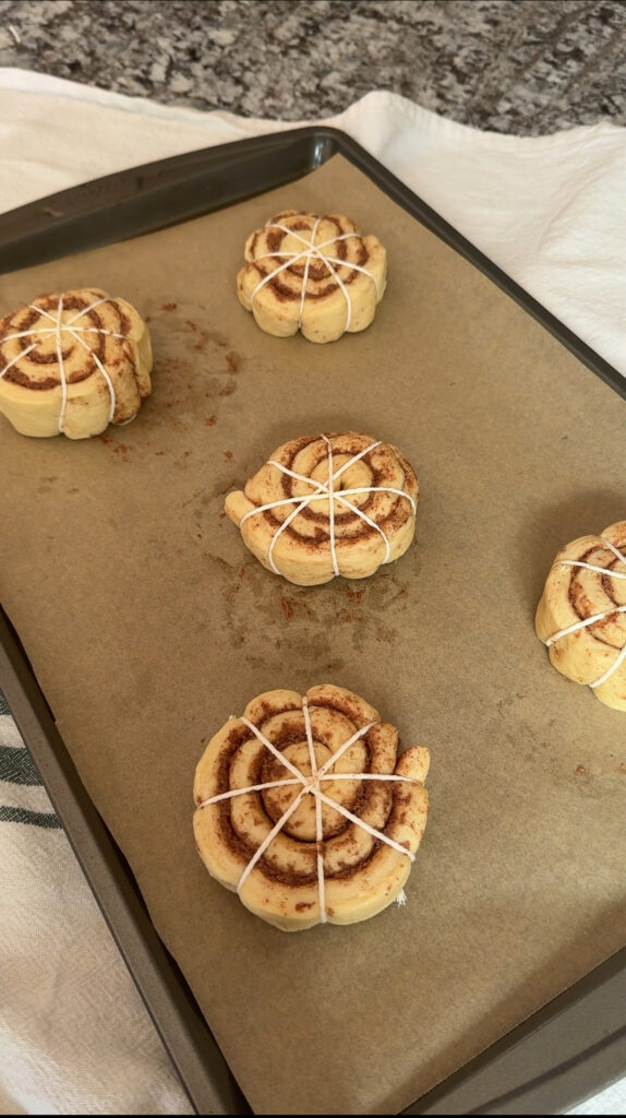 Raw cinnamon rolls tied with kitchen twine on a baking sheet